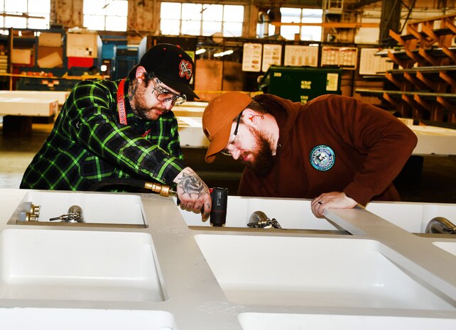 Norfolk Naval Shipyard’s Pipefitter Shop (Shop 56) Pipefitter Mechanic Patrick Douglas (left) and Helper-to-Worker Pipefitter Benjamin Roach work on the pipe assembly cooling system on a jet blast deflector,  a safety device on aircraft carrier flight decks to prevent damage and injury. “We take safety very seriously here in Shop 56. It has to be 100 percent perfect or we don’t sign off on it,” said Douglas. Roach added, “There’s just too much at risk for the Sailors on the flight deck that they need to have the confidence that the jet blast deflectors’ mechanical pieces will not fail them any time during flight operations.”