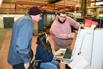 From left to right: Norfolk Naval Shipyard’s Pipefitter Shop (Shop 56) Pipefitter Dominick Bravo, Pipefitter Tammy Davenport and Pipefitter Tyler Bell collaborate while testing a pipe bending machine after receiving updated software.