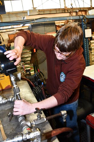 Norfolk Naval Shipyard’s Pipefitter Shop (Shop 56) Pipefitter Philip White is attaching a pressure gauge to a test rig. He is an apprenticeship graduate and has been working at the shipyard for eight years. “I became a pipefitter because I come from a long line of tradesmen and adding pipefitter knowledge expands my family's experience base,” said White.