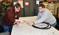 Norfolk Naval Shipyard’s Pipefitter Shop (Shop 56) Pipefitter Philip White (left) and Pipefitter George Sweeney are attaching a hose to a test rig to see if the hose meets all criteria for use. “Our test gang performs testing evolutions on most hoses and piping assemblies before installation on the ship,” said Sweeney.