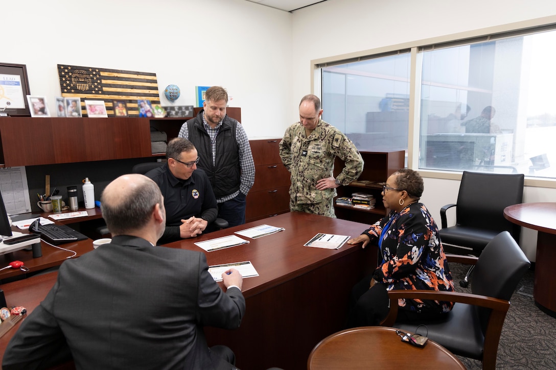 Four men and one woman surround a desk looking at papers on desk.
