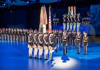 Army Soldiers in various uniforms are standing in formations in a large hall during a ceremony.