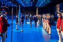 Army soldiers in various uniforms are standing in rows during a pass in review ceremony, as one Soldier is lead down in front of the troops to inspect them.