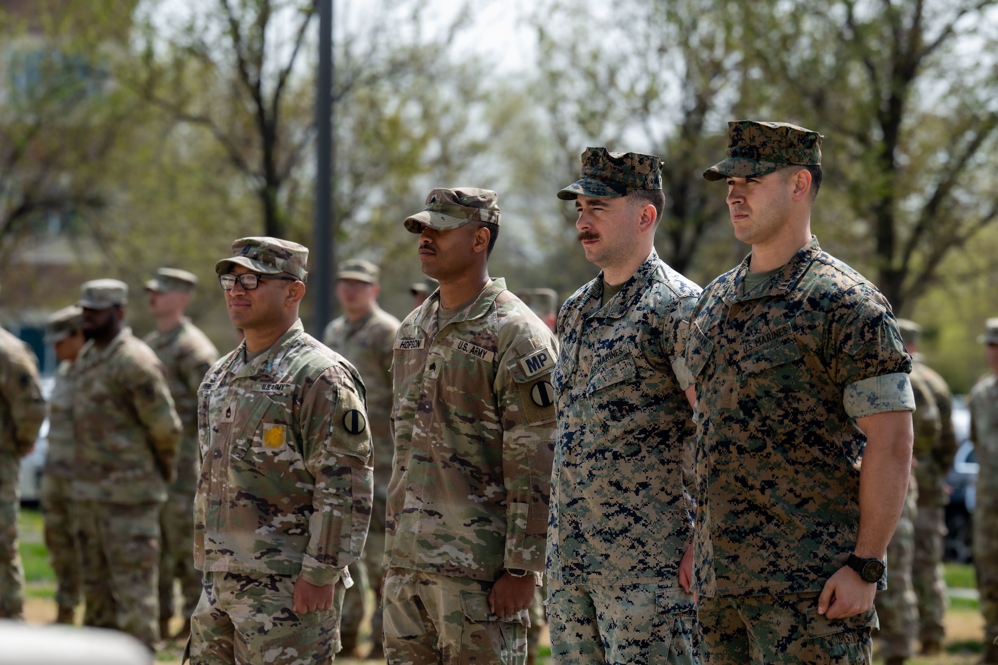 Four service members stand in a line and at attention outside.