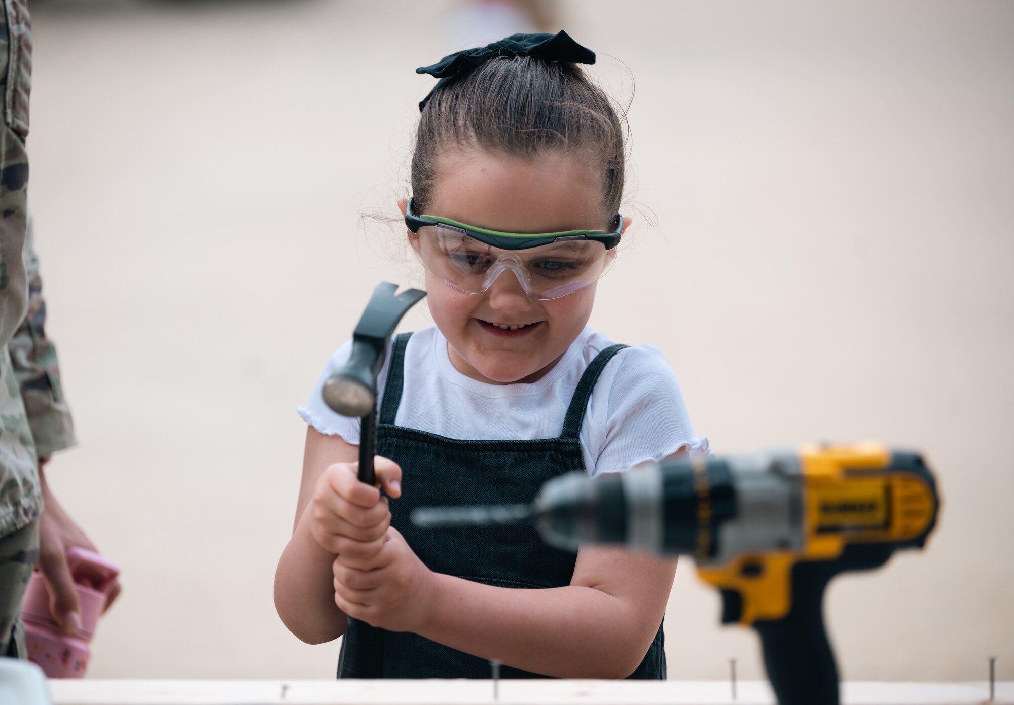 A little girl in a white shirt and black dress hammers a nail outside
