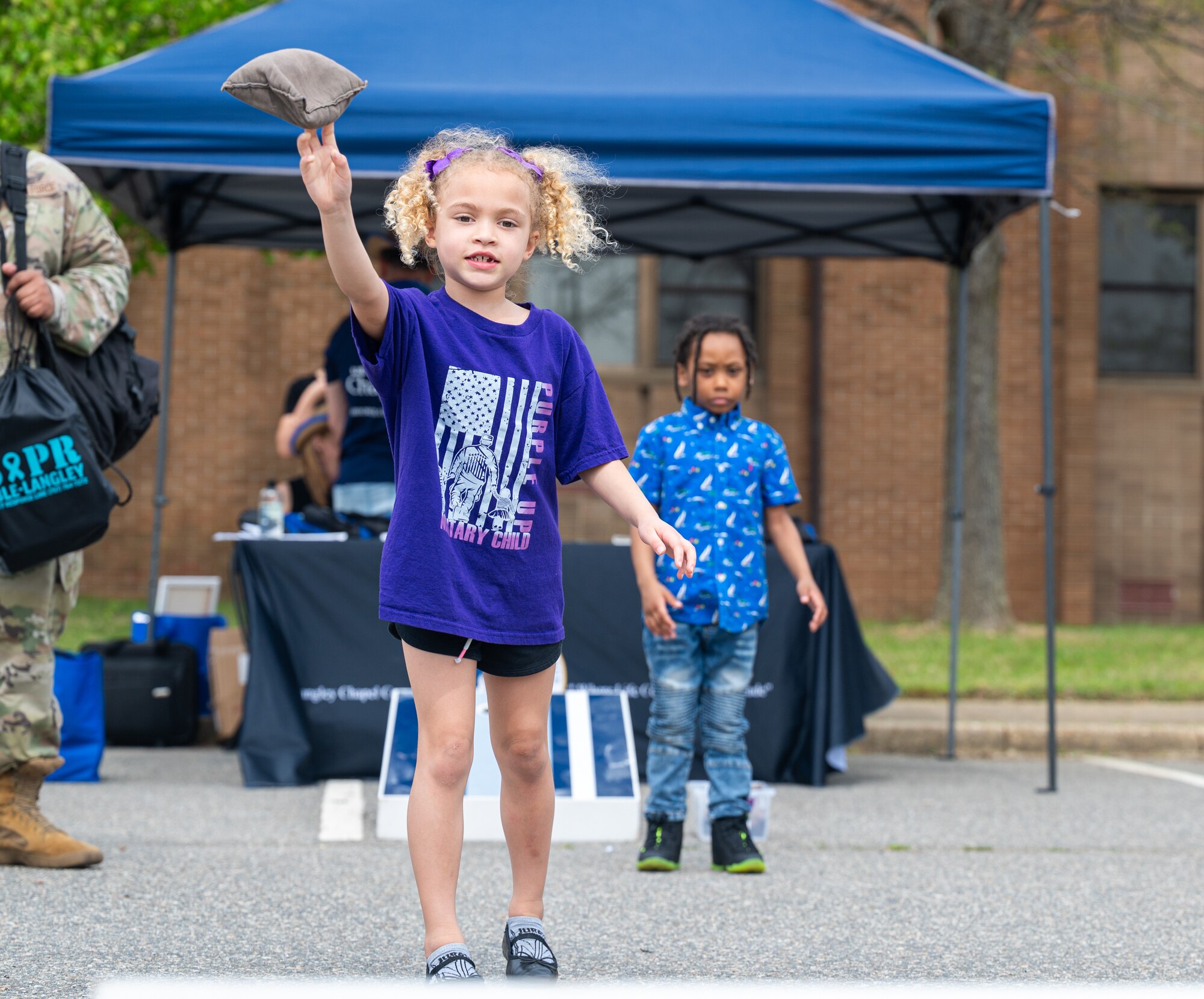 A girl with a purple shirt throws a bean bag outside