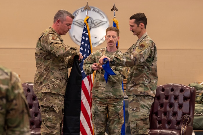 U.S. Air Force Lt. Col. Aaron Knight, former 355th Operations Support Squadron commander, right, rolls the 355th OSS guidon as Lt. Col. Patrick Chapman, 355th Operations Group deputy commander, left, prepares to sheath it during the 355th OSS inactivation ceremony at Davis-Monthan Air Force Base, Arizona, April 3, 2025. The sheathing of the guidon symbolized the inactivation of the squadron.
