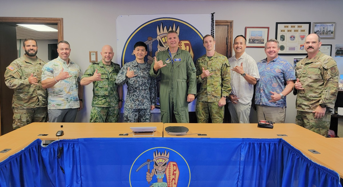 a mix of 9 soldiers and civilians med pose for a photo standing behind a conference table.