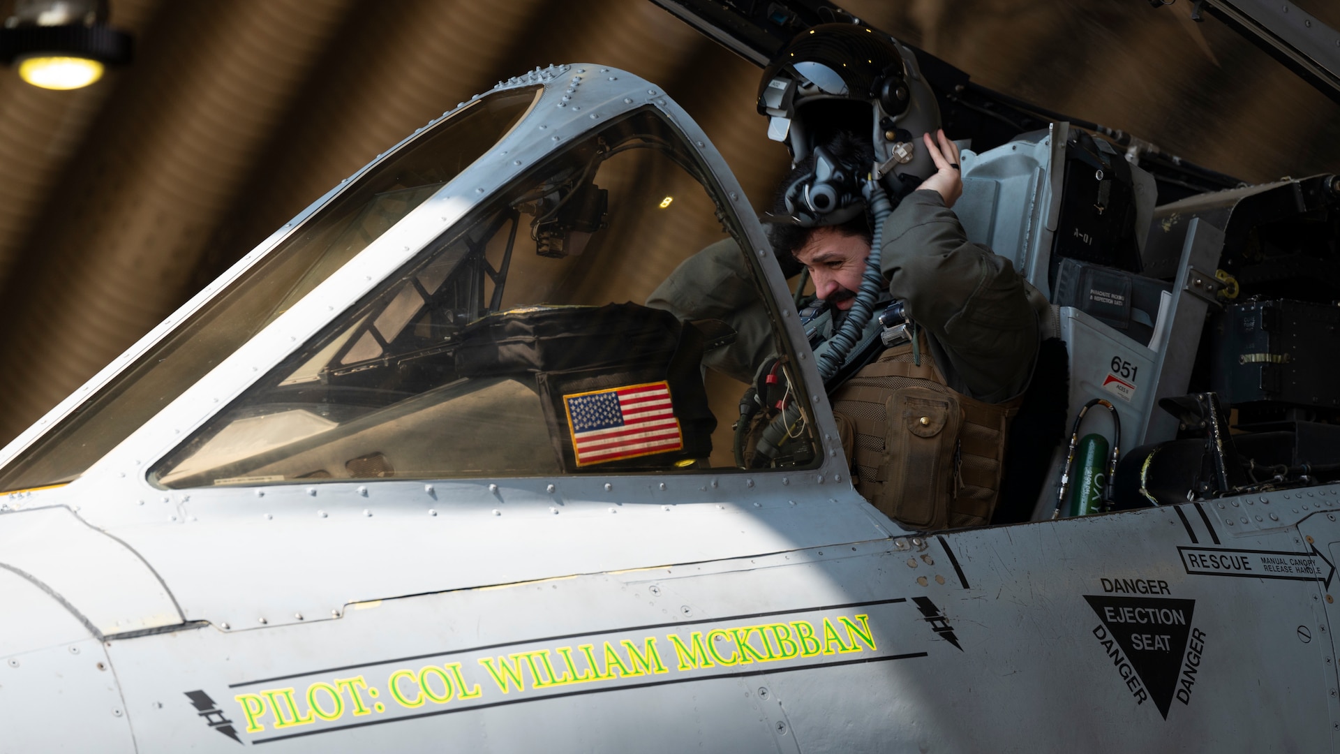 A pilot seated in an A-10 Thunderbolt cockpit puts his helmet on