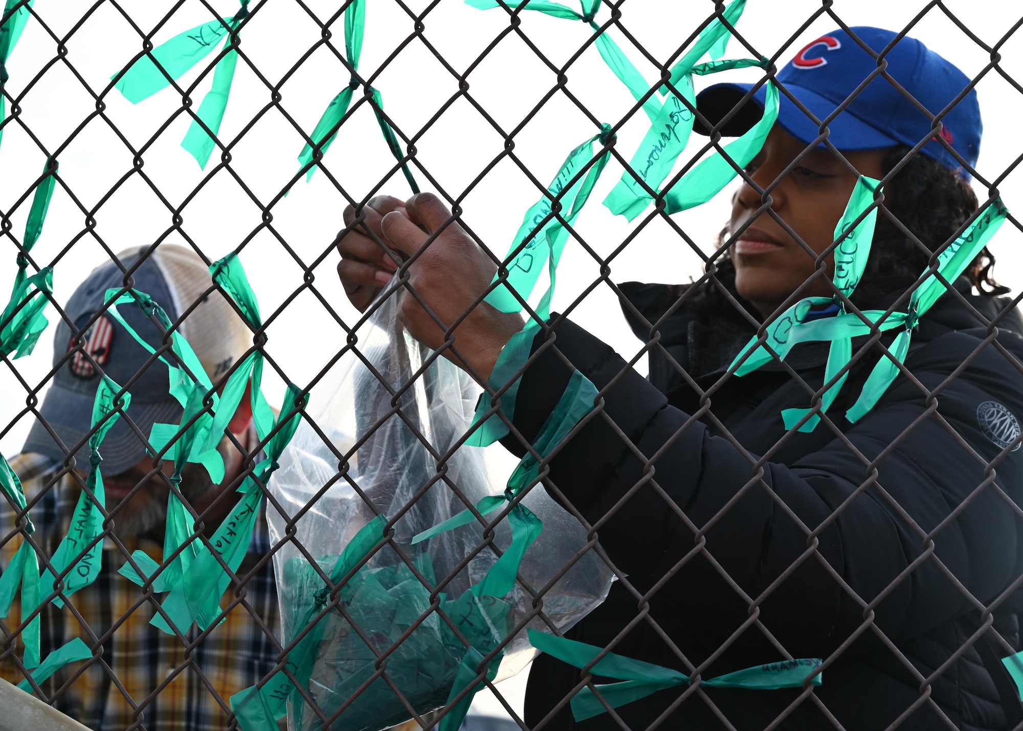 A man and a woman tying teak ribbon to a fence.