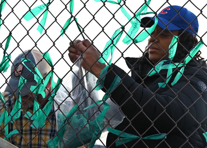 A man and a woman tying teak ribbon to a fence.