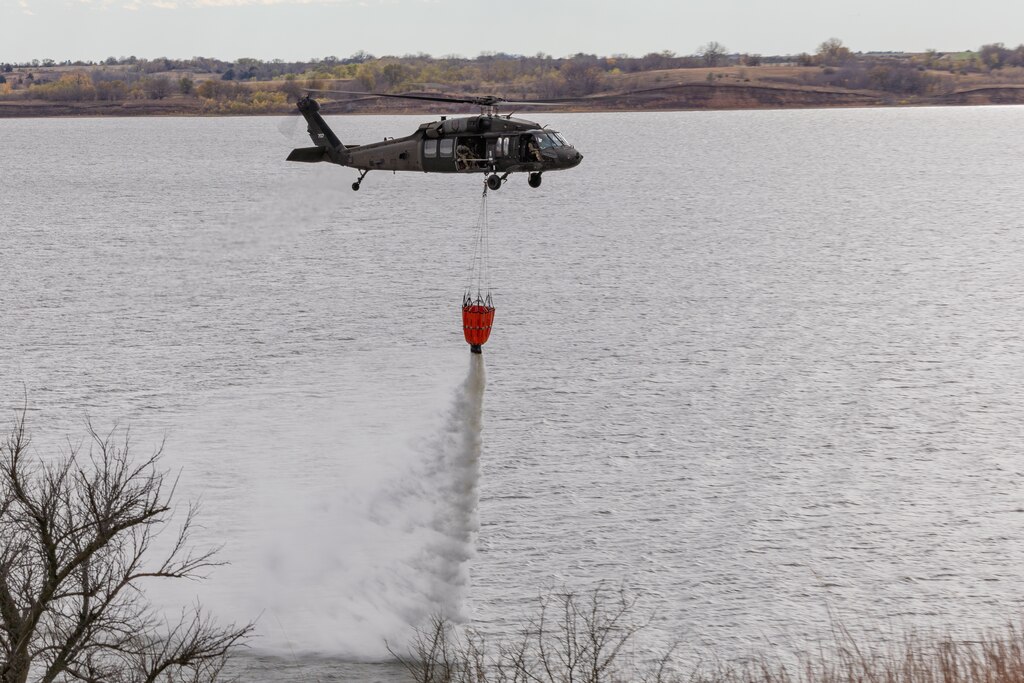 Military helicopter dumps water onto lake from underslung water bucket