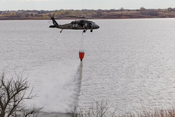 Military helicopter dumps water onto lake from underslung water bucket