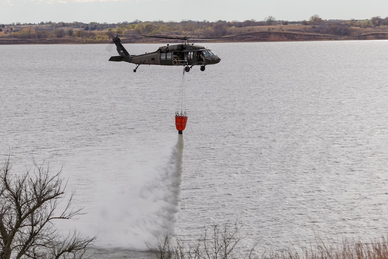 Military helicopter dumps water onto lake from underslung water bucket