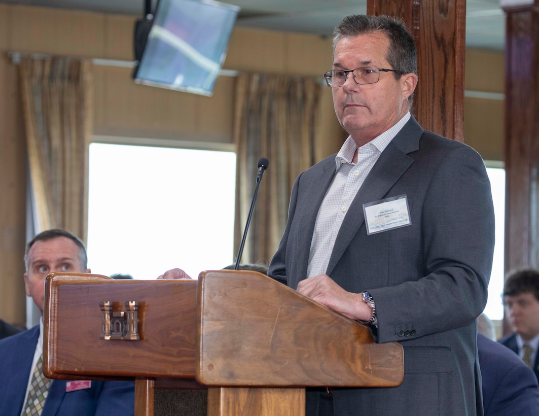 Man wearing blazer and glasses standing behind a podium.