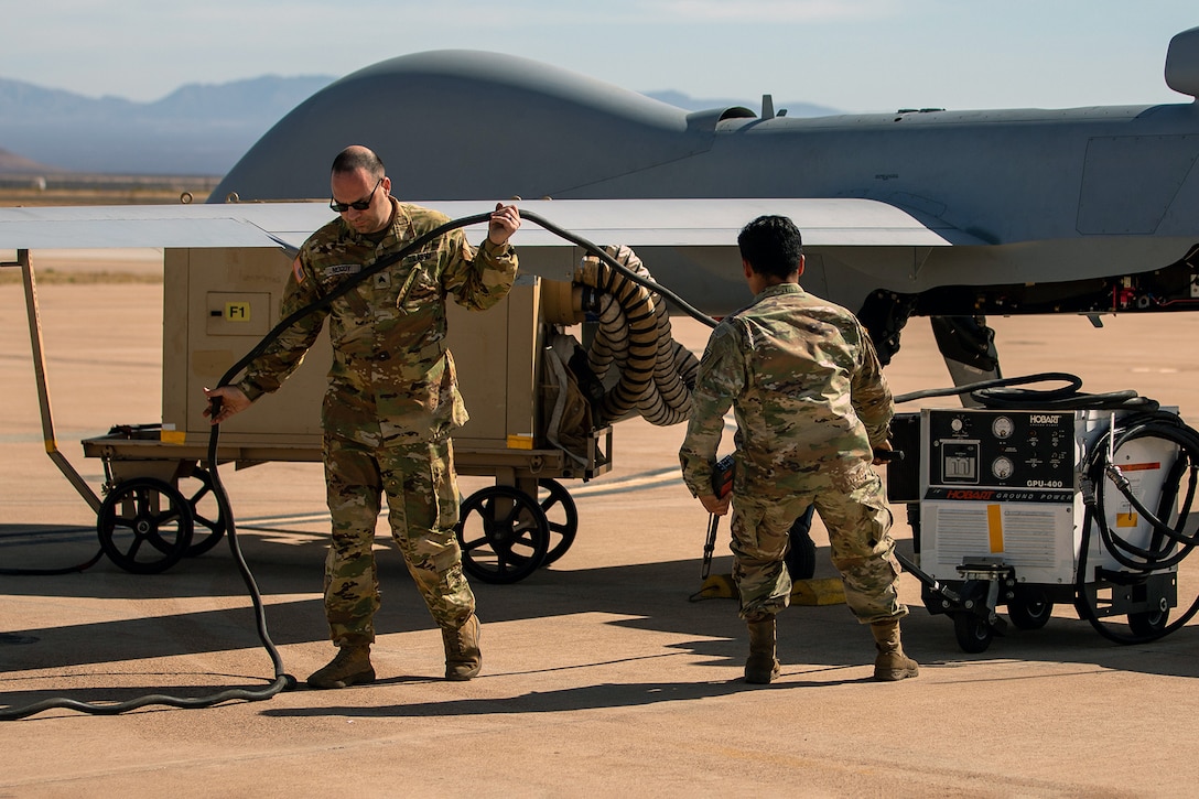 Two soldiers remove a generator from a large drone during the day.