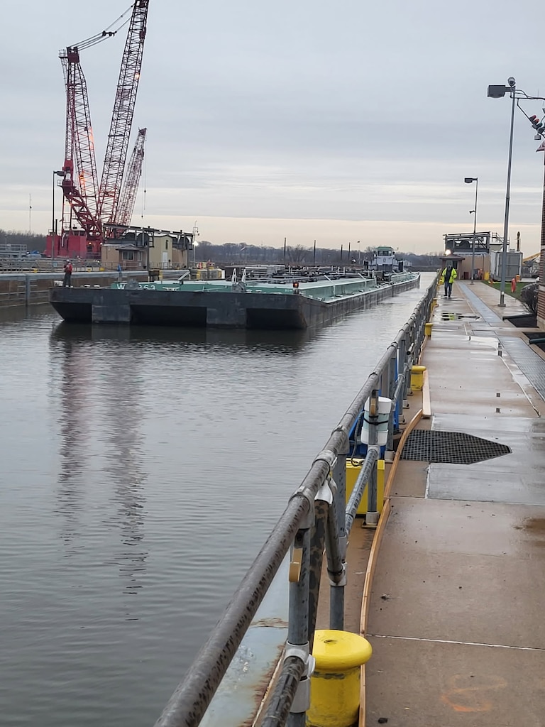 barge floating on river with construction cranes behind it.