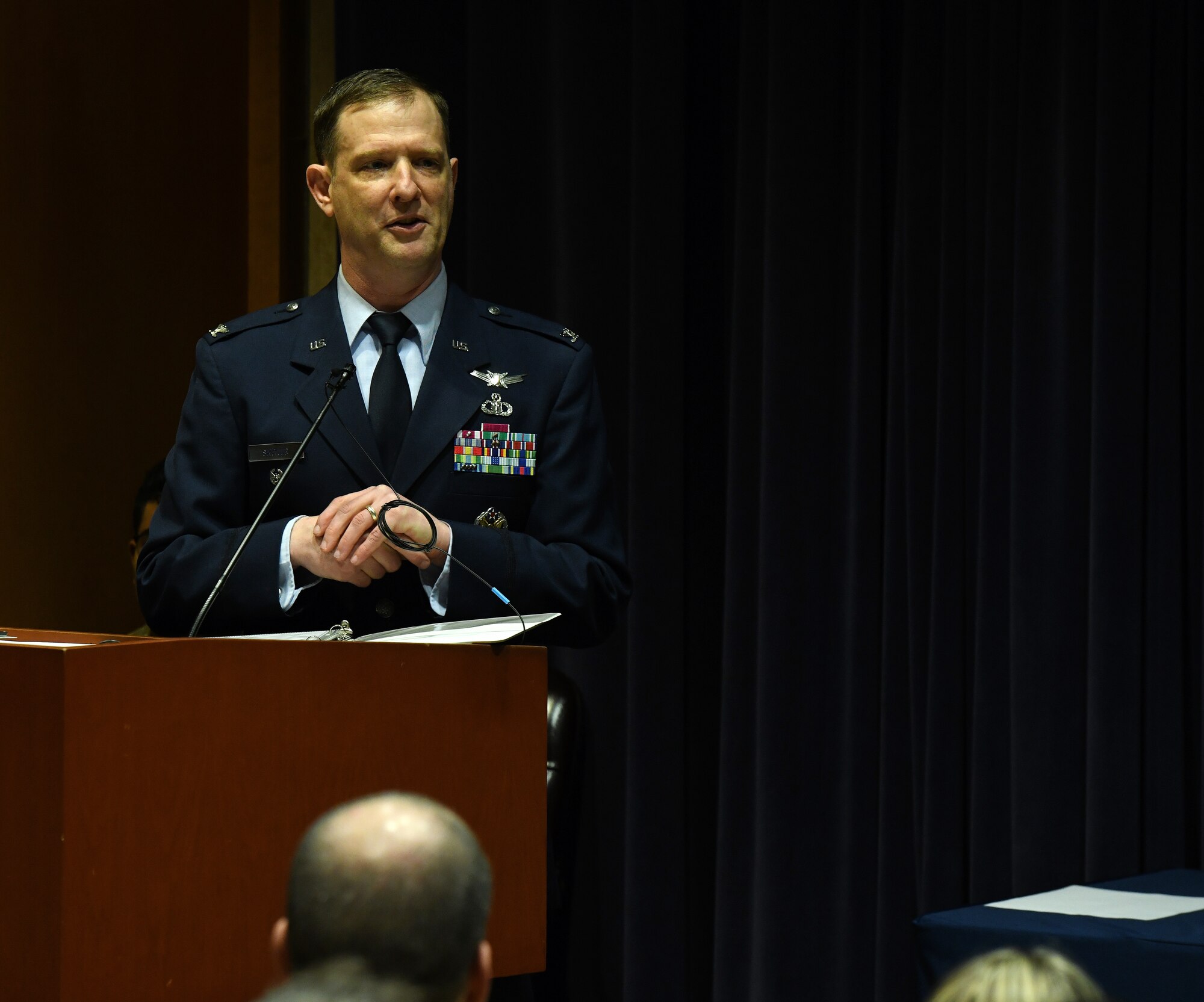 man in military dress uniform stands at a podium addressing an audience.