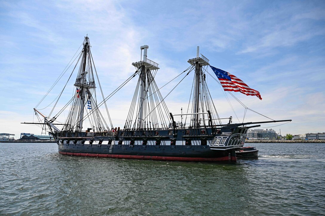A warship sails in a harbor on a partly cloudy day.