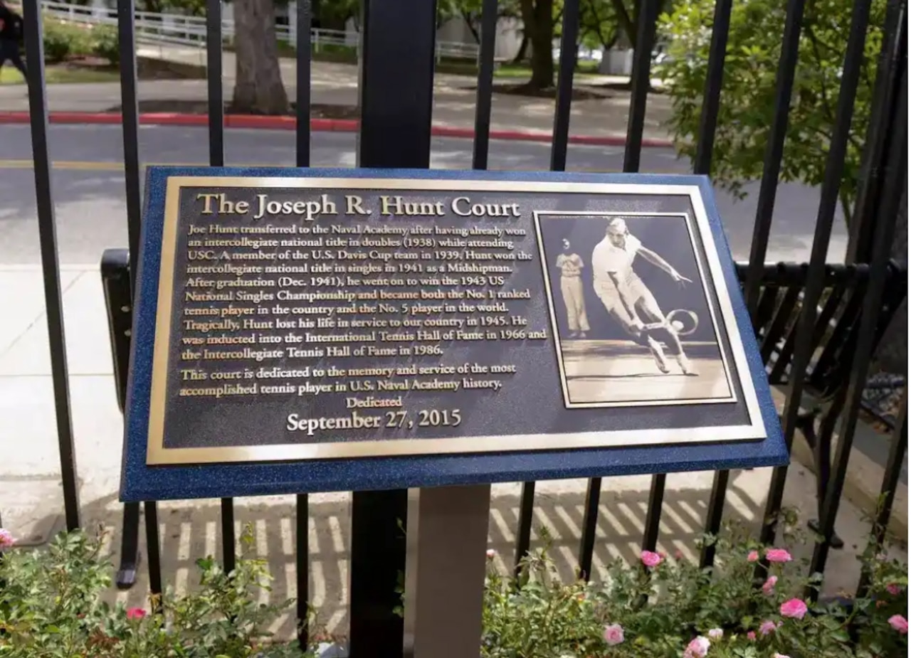 A plaque that reads “The Joseph R. Hunt Court” is shown outside in front of a fence.