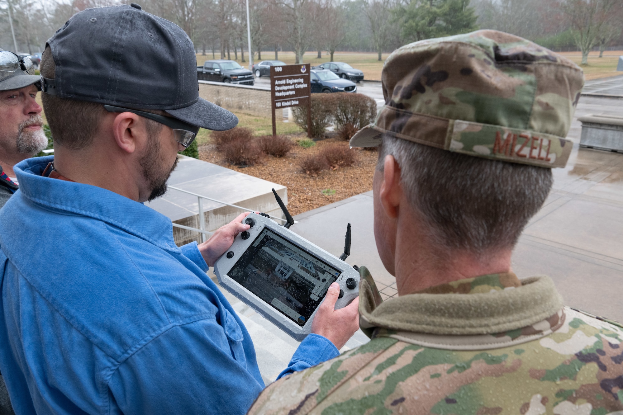 Arnold Engineering Development Complex Commander Col. Grant Mizell, right, takes a look at the image provided by the digital camera of a Small Unmanned Aircraft System, also known as an sUAS or a “drone,” during a March 5, 2025 demonstration of the device at Arnold Air Force Base, Tenn. Piloting the sUAS is Robert Hastings, sUAS operator, center, and Matt Holder, sUAS observer. The sUAS will soon be used at Arnold to perform asset health assessments. The device is equipped with both digital and infrared imaging capabilities and will be flown around installation buildings, plant facilities and associated equipment to ensure there are no compromises to such assets and to assess the structural integrity of facilities. (U.S. Air Force photo by Keith Thornburgh)