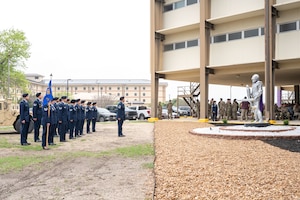A military unit is in formation in front of a knight statue and memorial plaque.