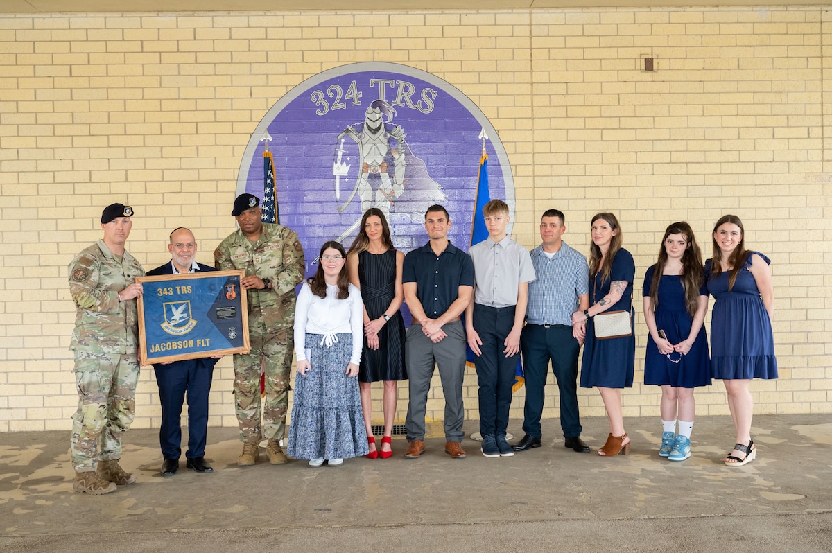 Two military members present a gift to a family in front of the 324th Training Squadron emblem