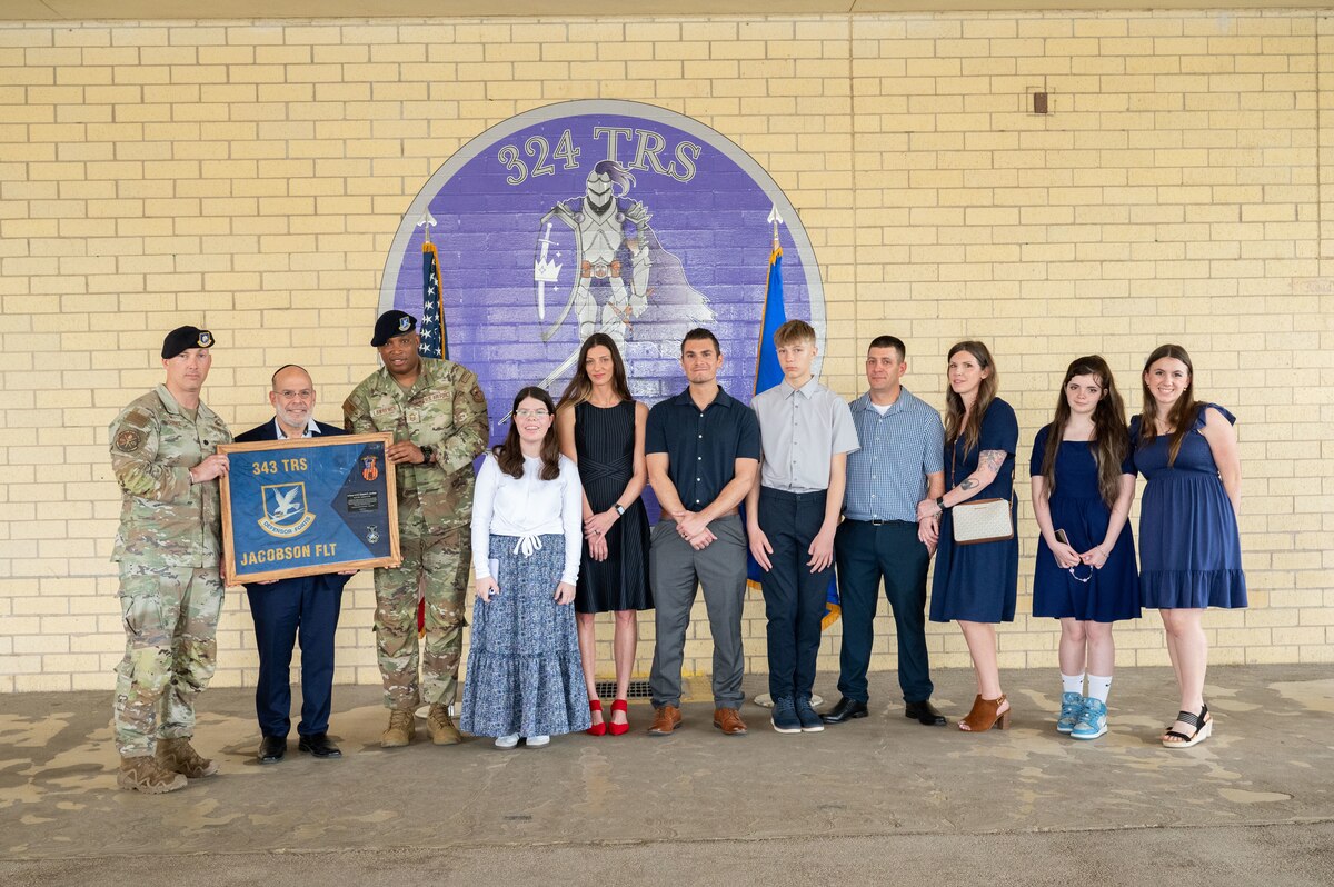 Two military members present a gift to a family in front of the 324th Training Squadron emblem