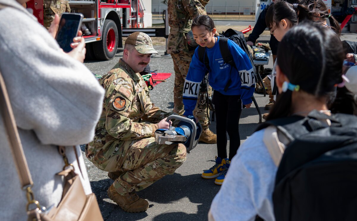 A U.S. Air Force Airman assigned to the 35th Civil Engineer Squadron fire station showcases a “Jaws of Life” recovery tool to children during Operation CODE (Children on Deployment Exercise) at Misawa Air Base, Japan, April 5, 2025. This event provides children with a firsthand look at military operations, strengthening the bonds that unite the 35th Fighter Wing community and enhance family resilience.  (U.S. Air Force photo by Senior Airman Brittany Russell)
