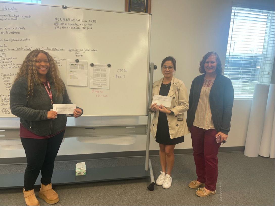 3 women pose next to a white board
