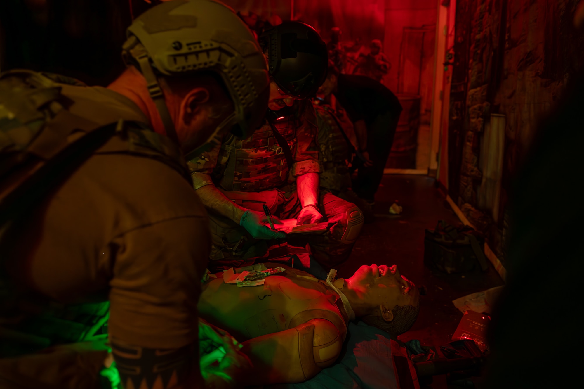Medical Airmen stabilize a casualty and document patient care in darkness with night vision flashlights.