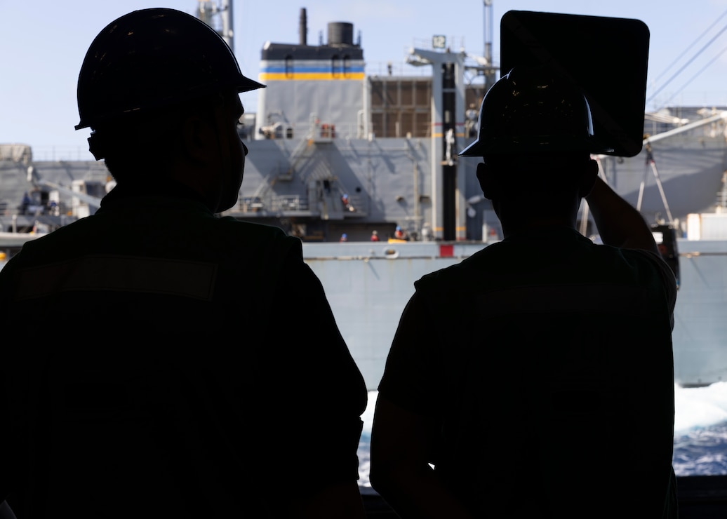 Boatswain’s Mate 3rd Class Ty Toporowki (left) and Boatswain’s Mate Seaman Gerber PelicoGonzalez, both assigned to deck department aboard the world’s largest aircraft carrier, USS Gerald R. Ford (CVN 78), signal to the fast combat support ship USNS Supply (T-AOE-6) in the hangar bay during a replenishment-at-sea, April 4, 2025.