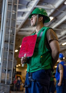 Boatswain’s Mate Seaman Gerber PelicoGonzalez, assigned to deck department aboard the world’s largest aircraft carrier, USS Gerald R. Ford (CVN 78), signals to the fast combat support ship USNS Supply (T-AOE-6) in the hangar bay during a replenishment-at-sea (RAS), April 4, 2025.