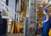 Boatswain’s Mate 3rd Class Chris Bustos, assigned to deck department aboard the world’s largest aircraft carrier, USS Gerald R. Ford (CVN 78), holds a line in the hangar bay during a replenishment-at-sea (RAS), April 4, 2025.