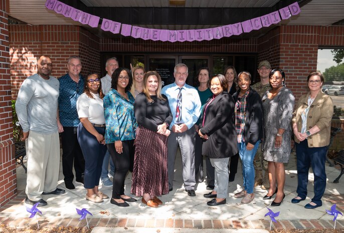Military and family readiness center workers standing in front of red brick building, multi cultured team members posing for a portrait photo.