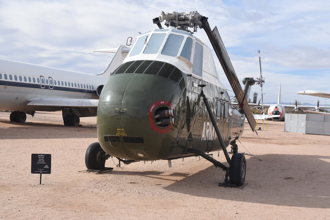 A helicopter is on display in a dirt field with aircraft to the left and behind it.