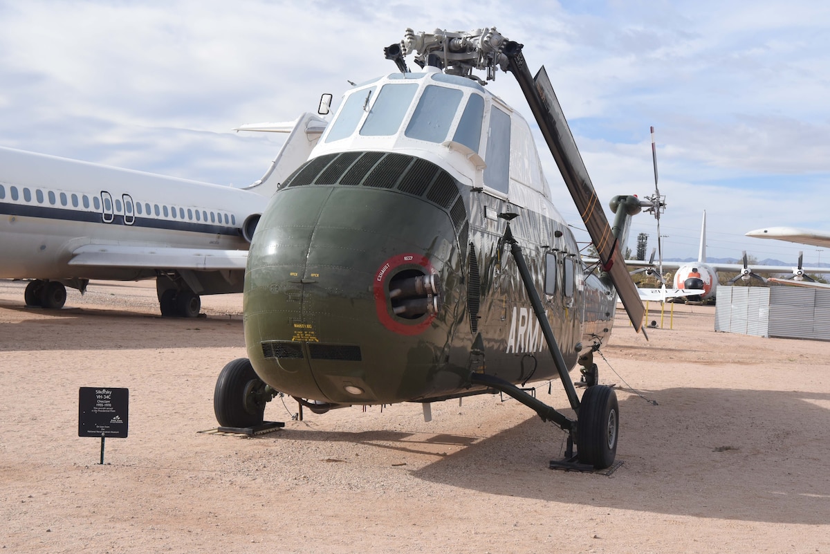 A helicopter is on display in a dirt field with aircraft to the left and behind it.
