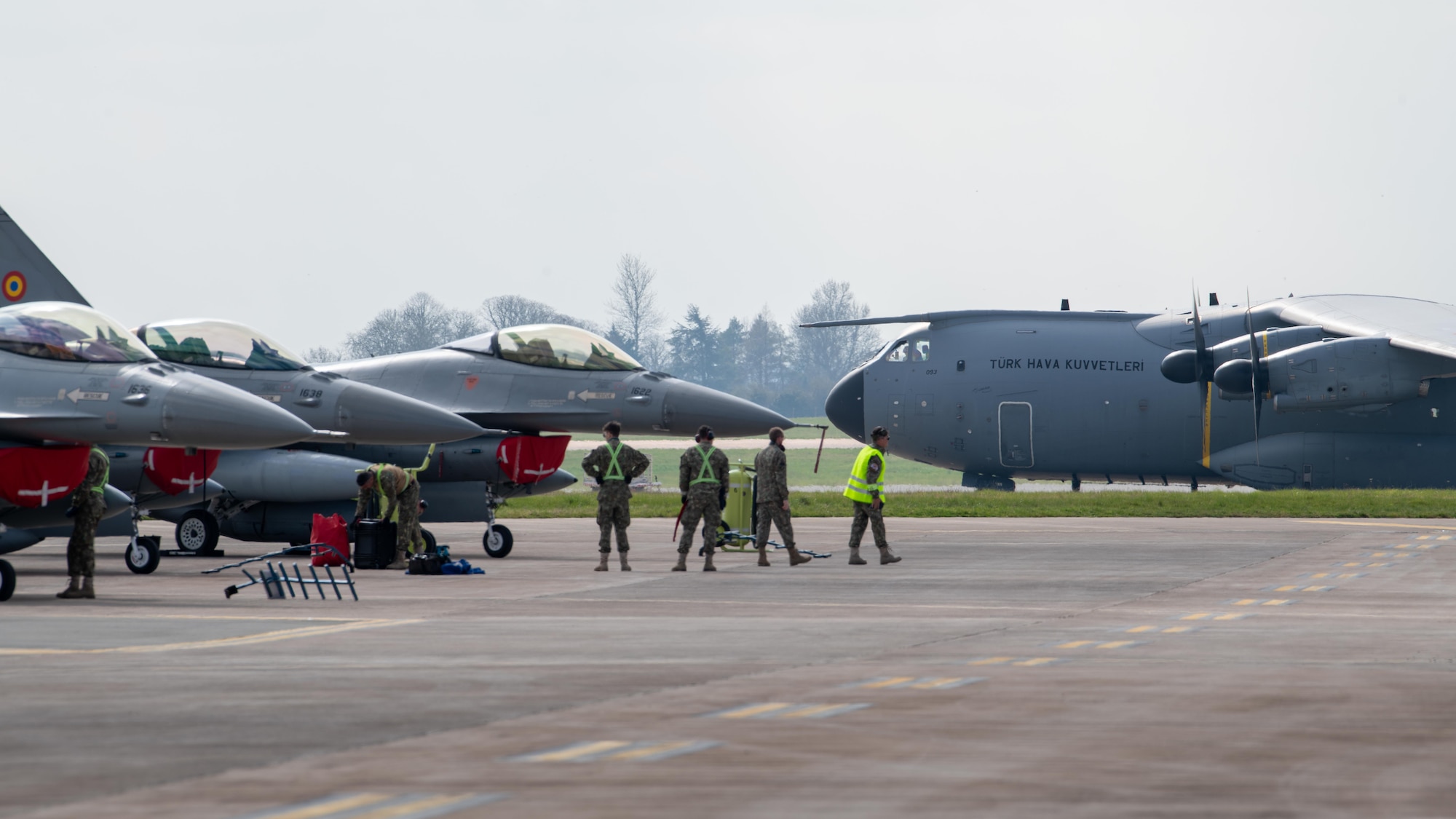 A Turkish Air Force (THK) Airbus A400M Atlas military transport aircraft taxis past three Romanian Air Force (RoAF) F-16AM Fighting Falcons