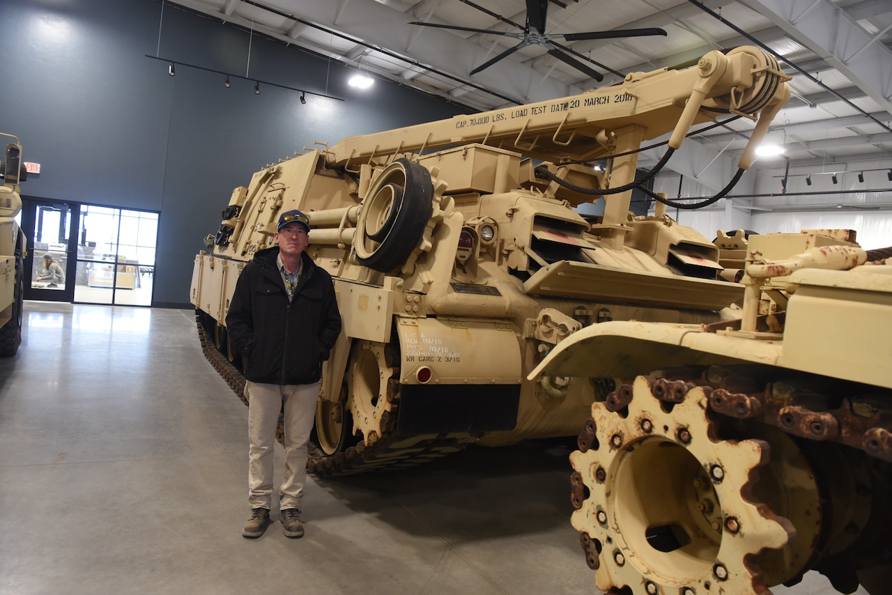 A man stands beside a military vehicle while inside a large building.