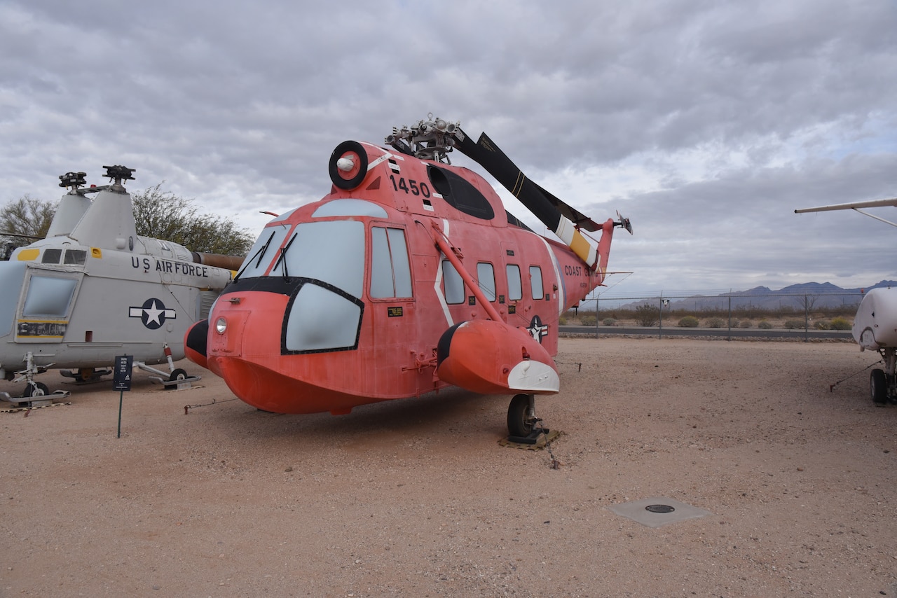 A helicopter is on display in a dirt field with an aircraft on the left.