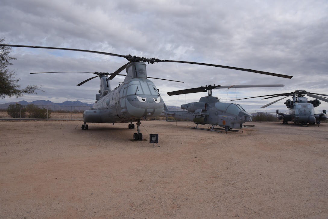 A helicopter is on display in a dirt field with two helicopters on the right.