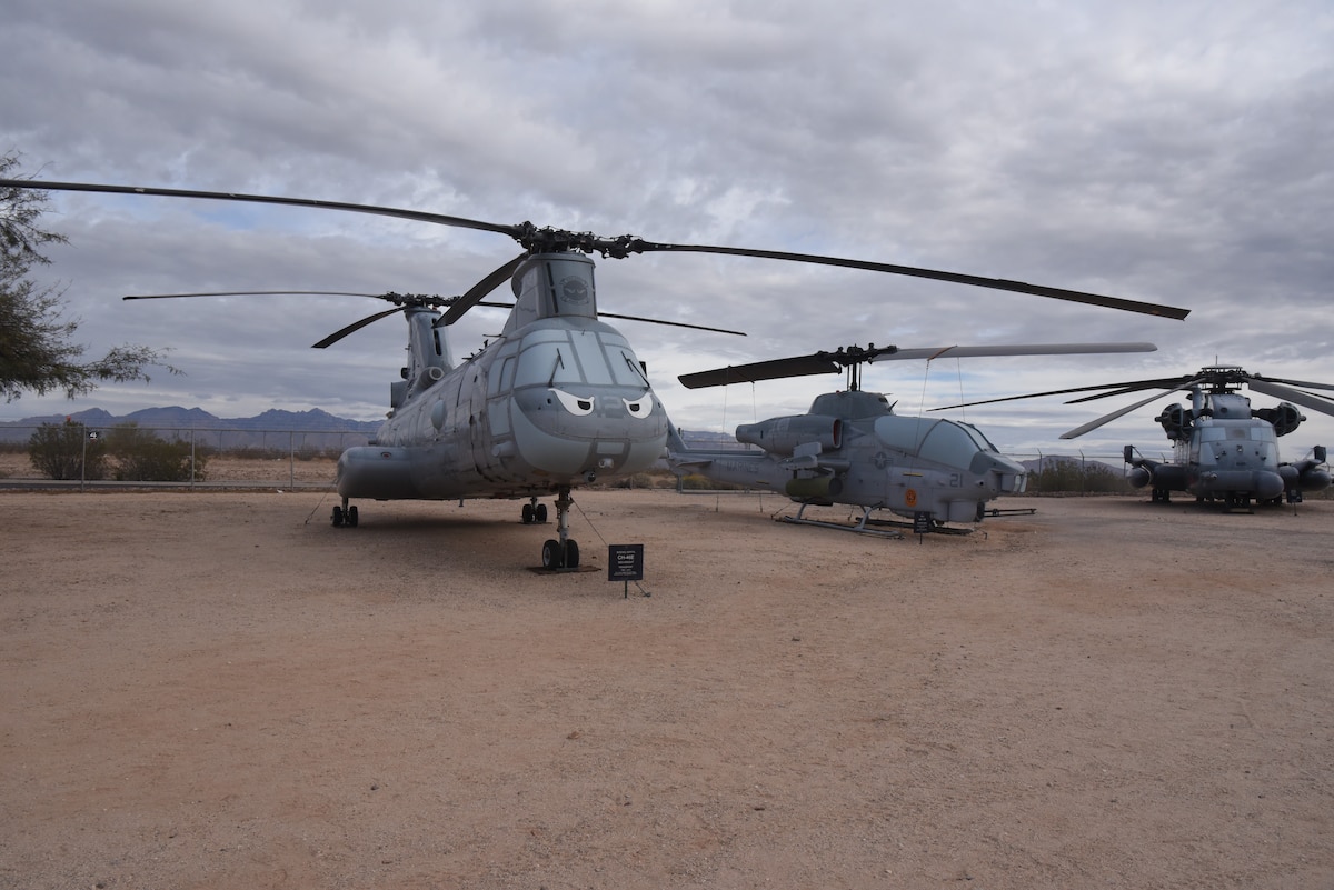 A helicopter is on display in a dirt field with two helicopters on the right.