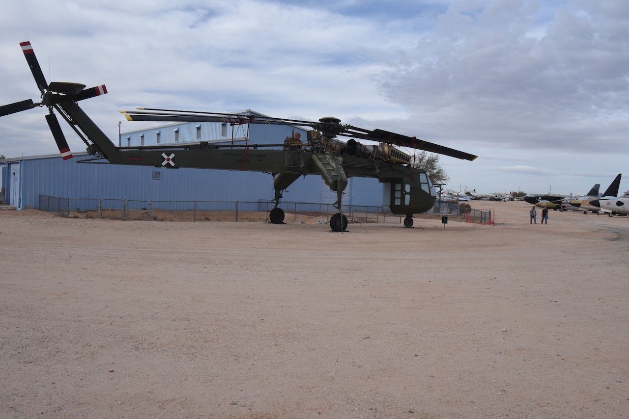 A helicopter is on display in a dirt field with a large building in the background.