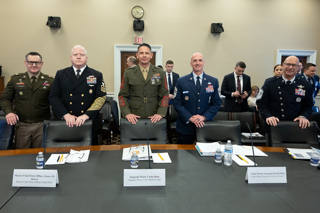 A group of five men in military dress uniforms are standing at a large table with their hands on leather chairs while posing for the camera.