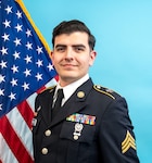 SGT Enriquez posing in his Army Service Uniform with the United States flag and blue background.