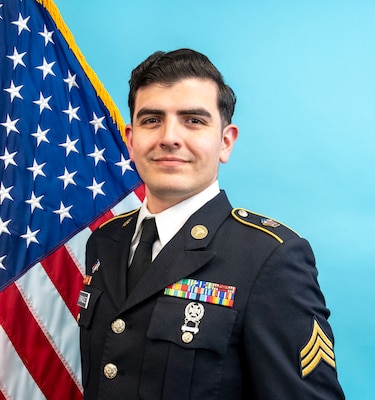 SGT Enriquez posing in his Army Service Uniform with the United States flag and blue background.