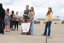 A family stands with a sign to greet their father at Beale Air Force Base, California, as he returns home after a six-month deployment, April 7, 2025.