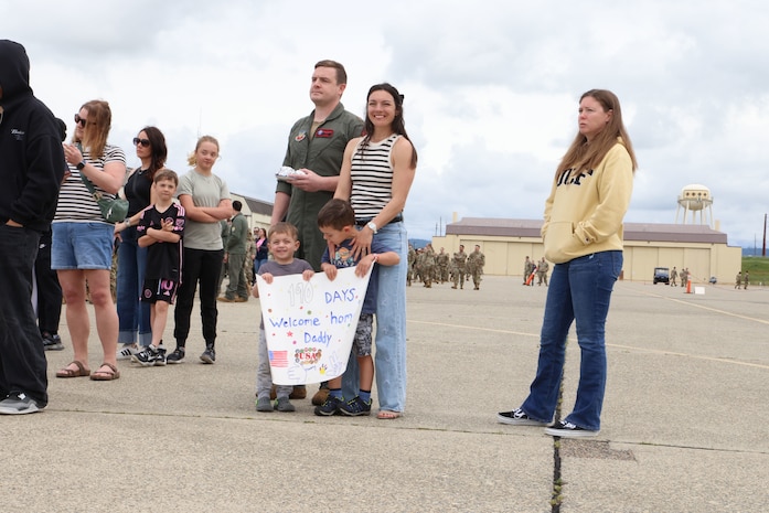 A family stands with a sign to greet their father at Beale Air Force Base, California, as he returns home after a six-month deployment, April 7, 2025.