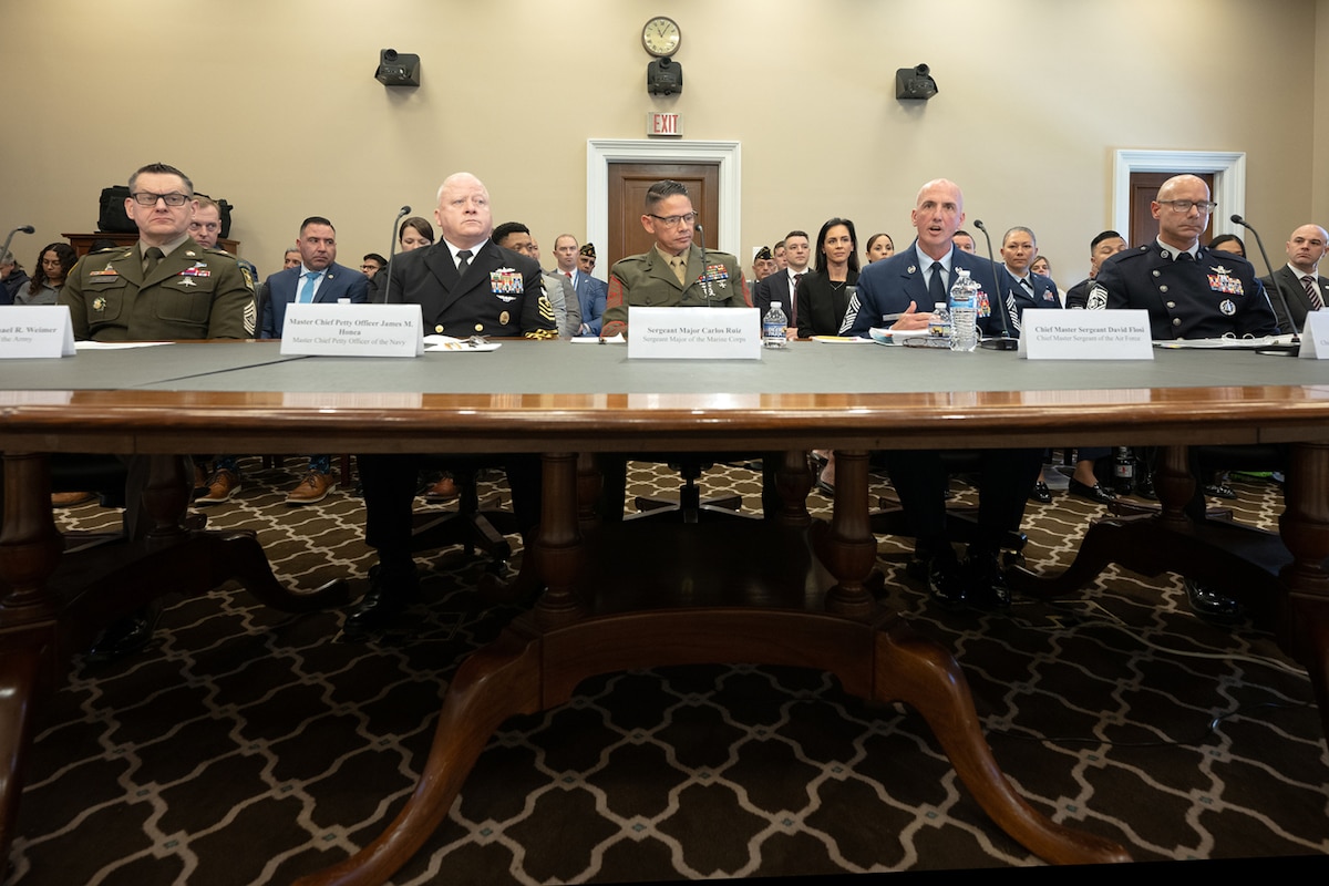 A group of five men in military dress uniforms are sitting at a large table speaking into microphones.