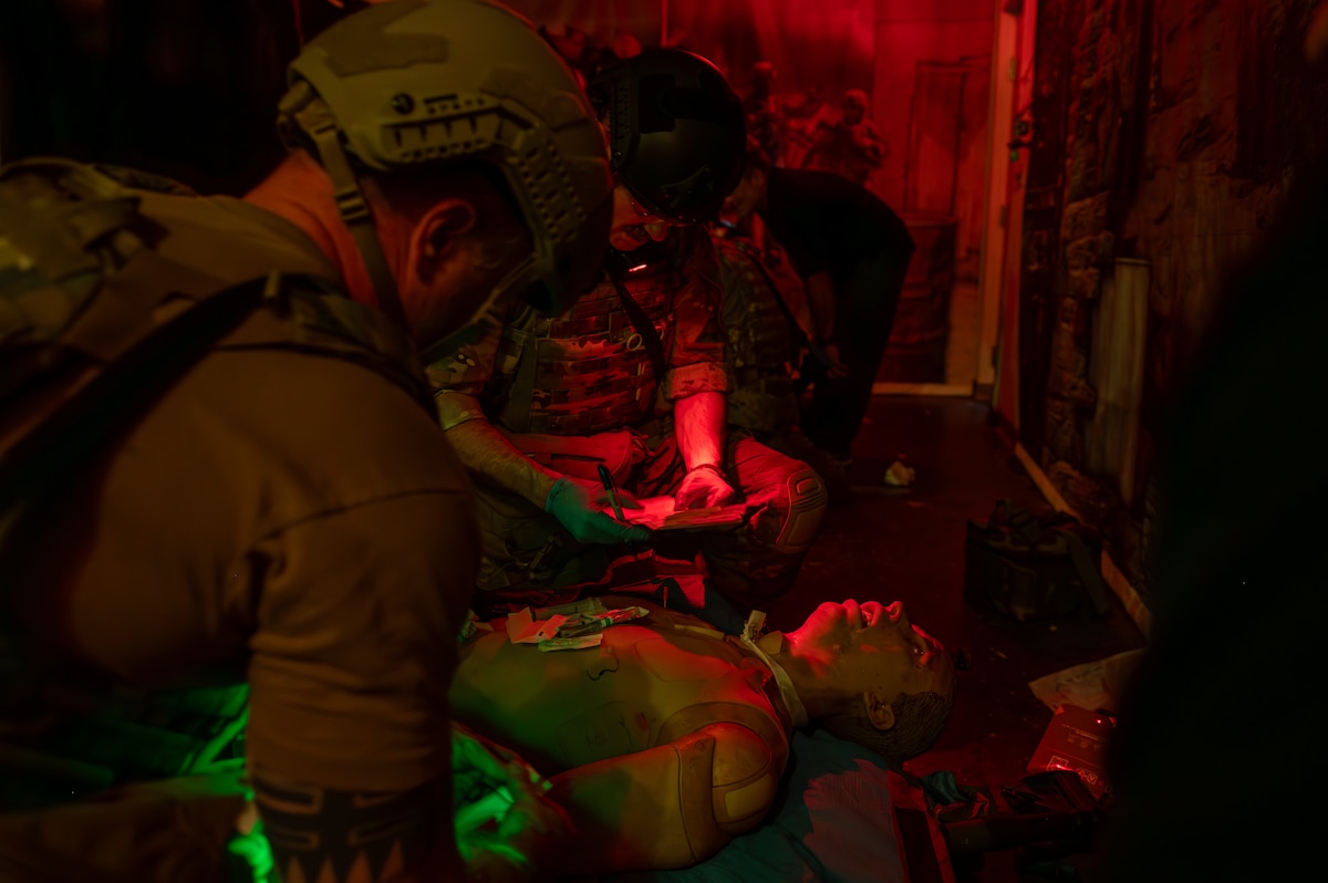 Medical Airmen stabilize a casualty and document patient care in darkness with night vision flashlights.